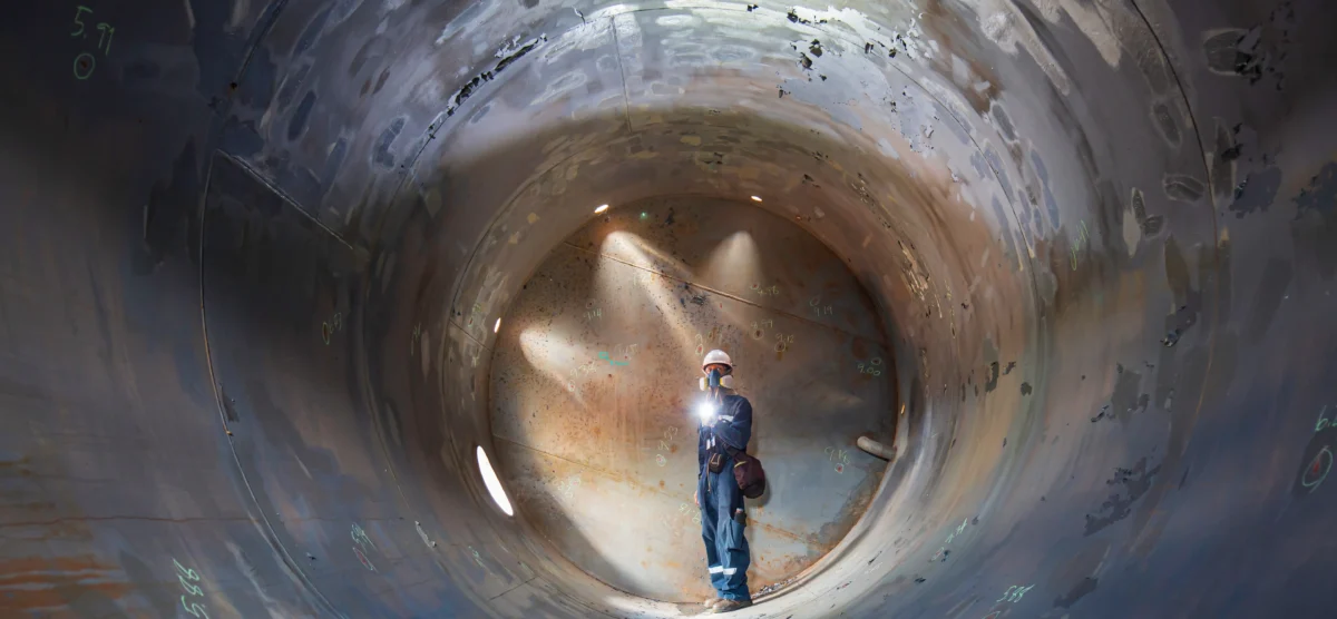Worker performs confined space maintenance inside an industrial pressure vessel.