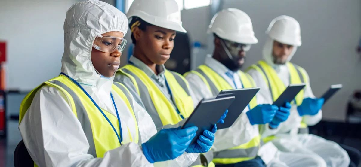 New workers in protective gear use tablets for digital onboarding during a group safety session.
