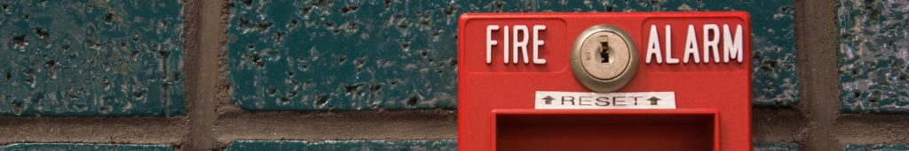 Red fire alarm on a blue brick building, illustrating the importance of fire prevention techniques.