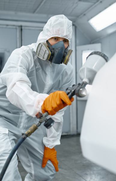 Technician hand in safety clothing spraying paint and varnish on car body part