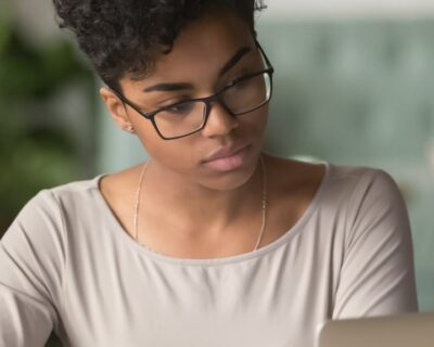 Horizontal photo banner for website header design, African student girl wear glasses sit indoors look at pc screen study on-line, do assignment, prepare for university admission exams, e-study concept