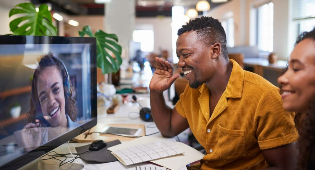 A Black man waves to his colleague on a video call from his office. High quality photo