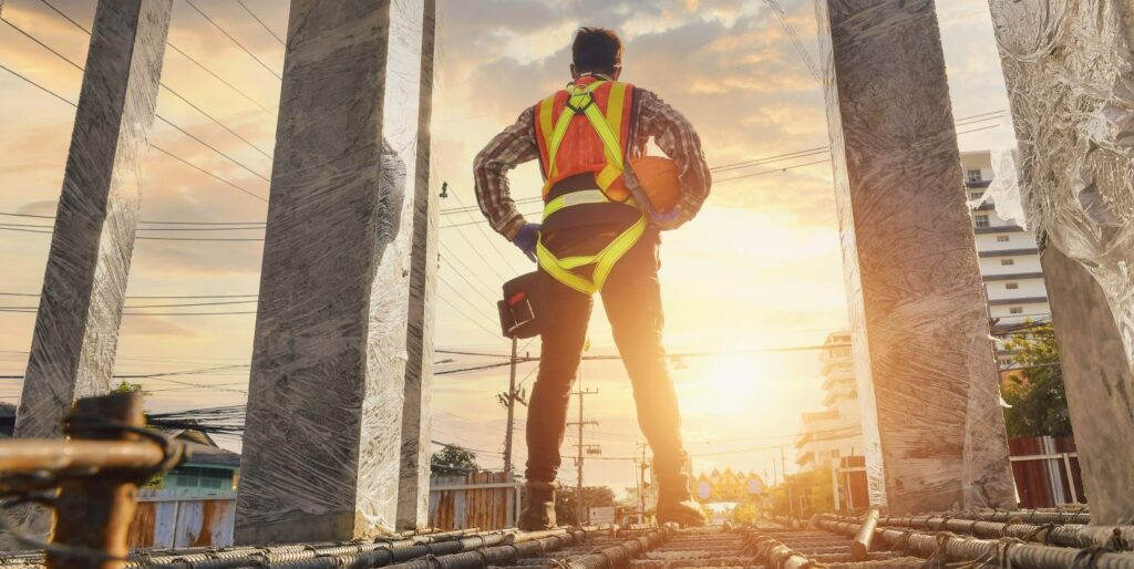 Construction specialist wearing safety work at high uniform on scaffolding at a construction site during sunset.