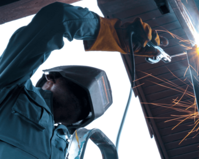 A welder works safely at his workplace while sparks and other debris protrudes from his torch.