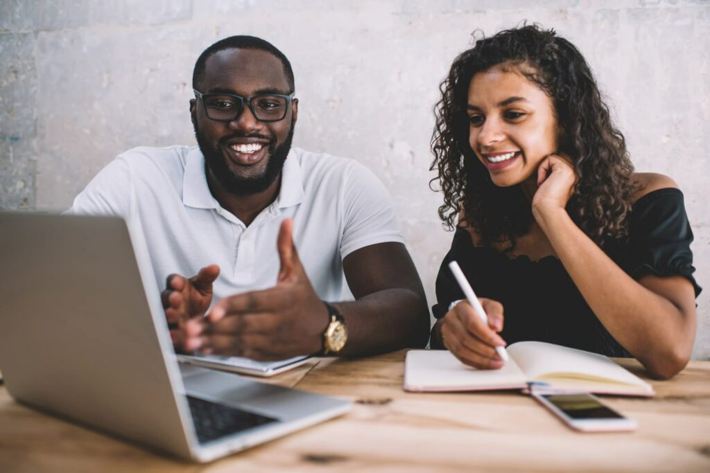 Cheerful african american male and female colleagues discussing learning management system on laptop computer, smiling dark skinned man explaining information to female student