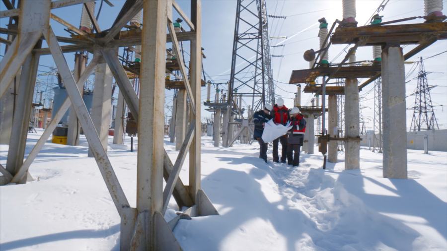 Engineers at electrical substation in winter. Action. Engineers and electricians look at electrical substation plan in winter. Working electrical substation on clear winter day.