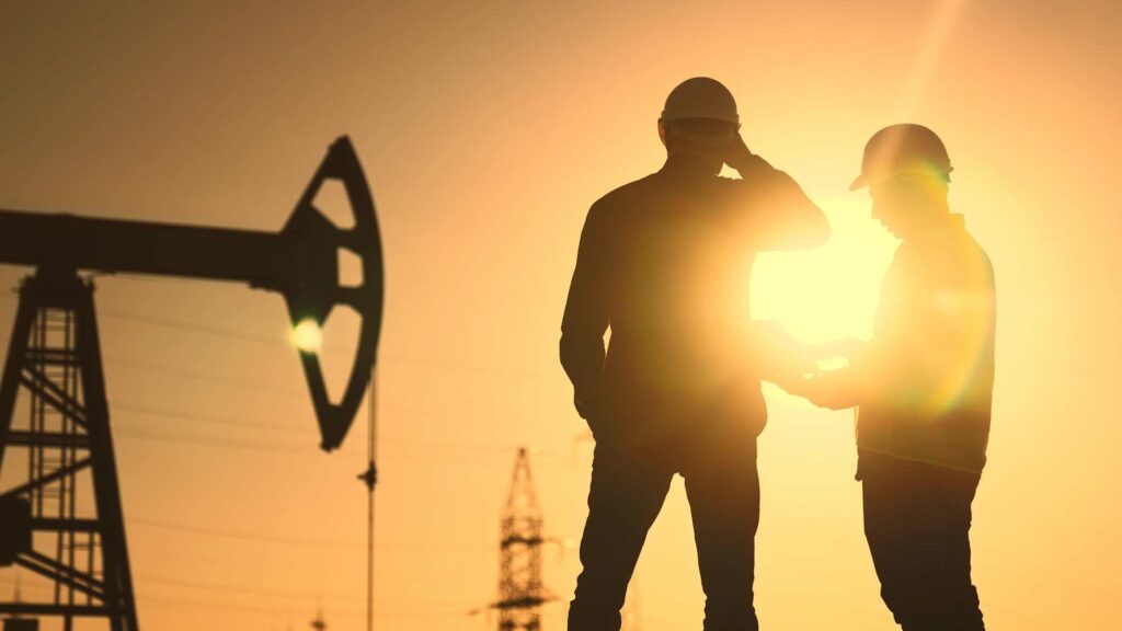 oil production. two silhouette workers work as a team next to an oil pump. business oil production production concept. two engineers of the oil and gas industry are sun discussing business plan