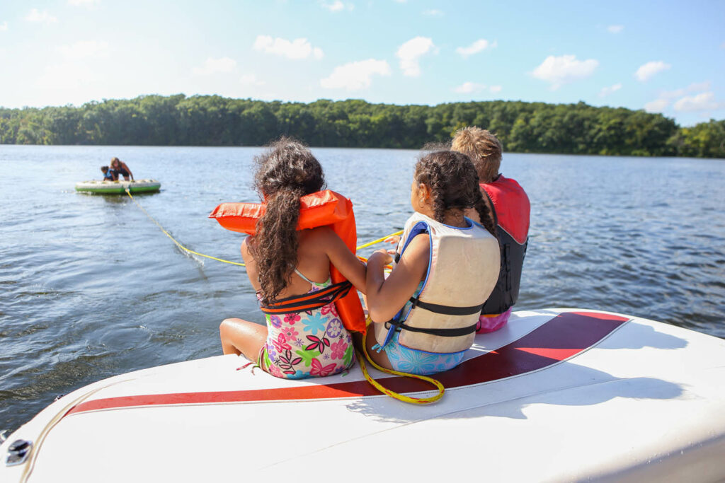 children on the end of a boat pulling a friend in on a tube.