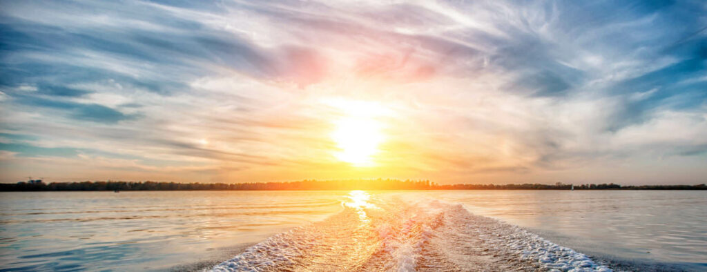 Boat wake and beautiful sunset casting yellow rays across the water