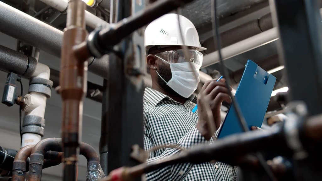 Industrial worker in PPE conducting a safety inspection with a clipboard inside a facility.