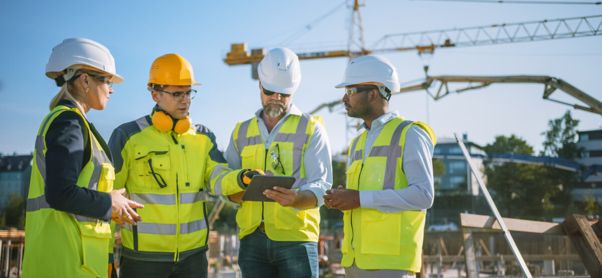 Worker in safety gear checking digital checklist on tablet at an active jobsite.